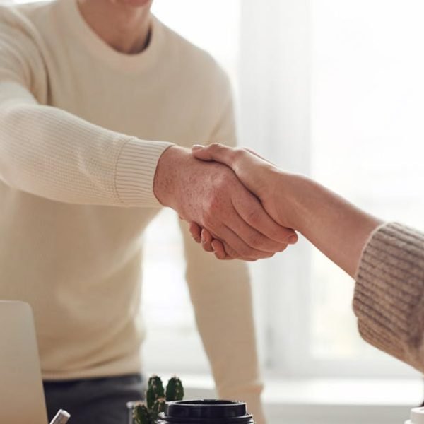 Close-up of professionals shaking hands over coffee in a modern office.