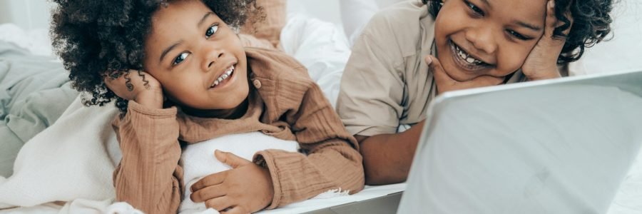 Two happy children lying in bed enjoying a movie on a laptop, embracing digital leisure lifestyle.