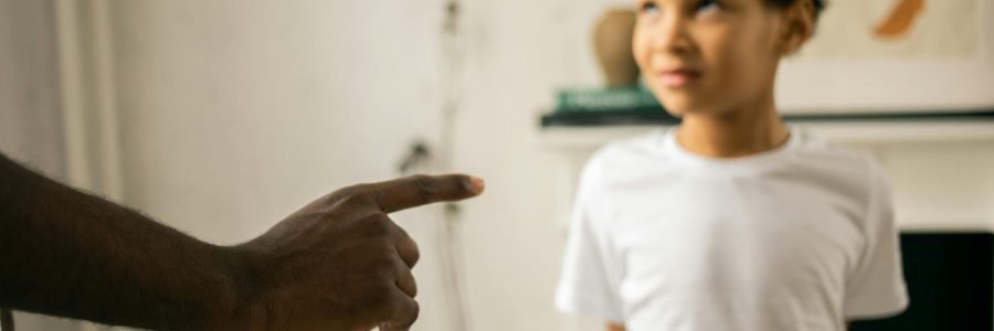 A father points and scolds his son indoors, emphasizing discipline.