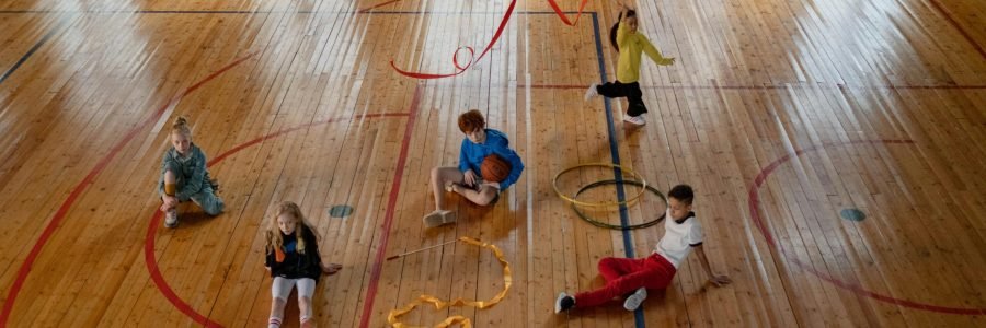 Children playing various games in an indoor gym with wooden floors, showcasing recreational fun.